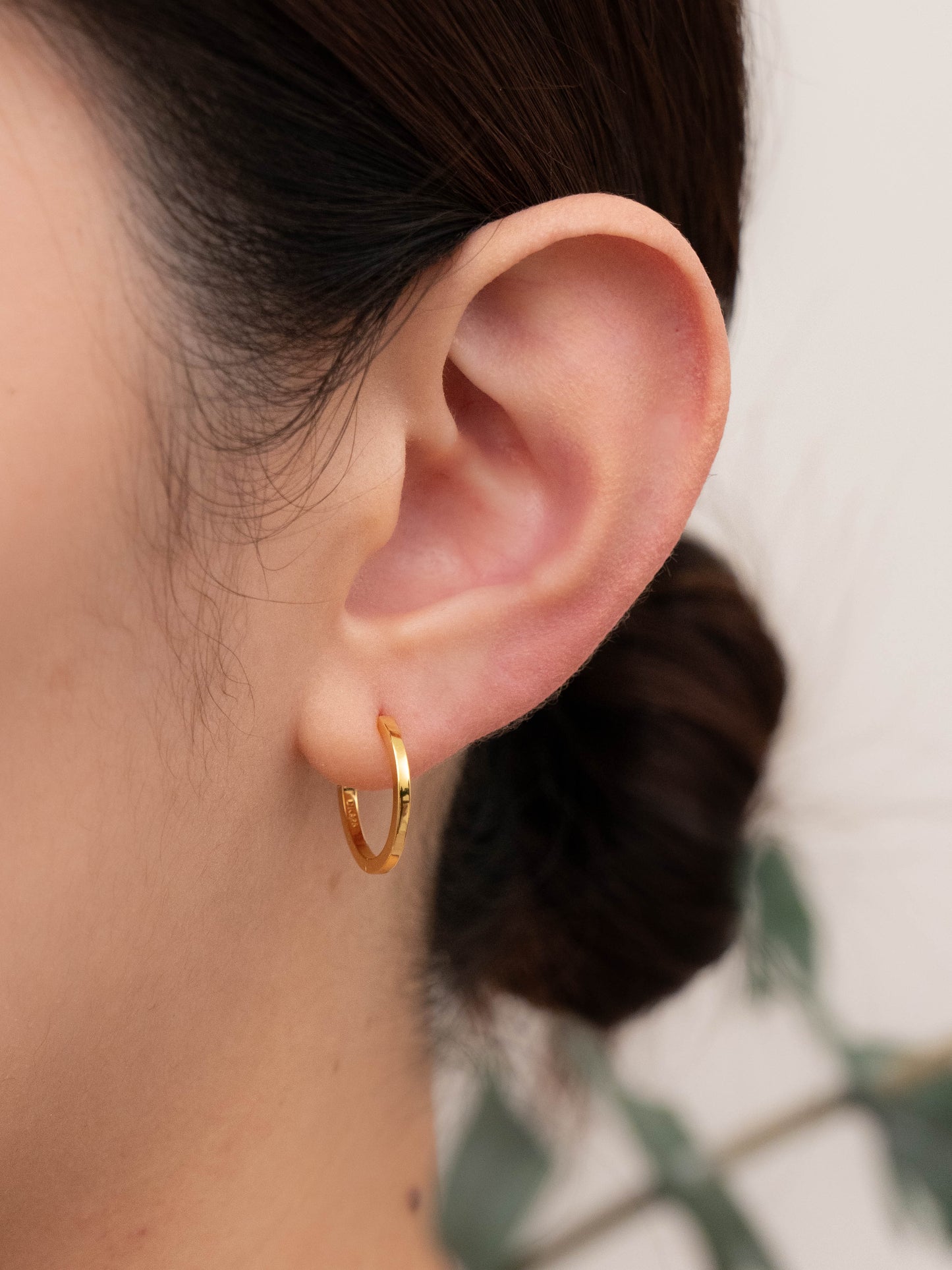 Small huggies gold on a model's ear, showing hinged closure and how they look when worn.