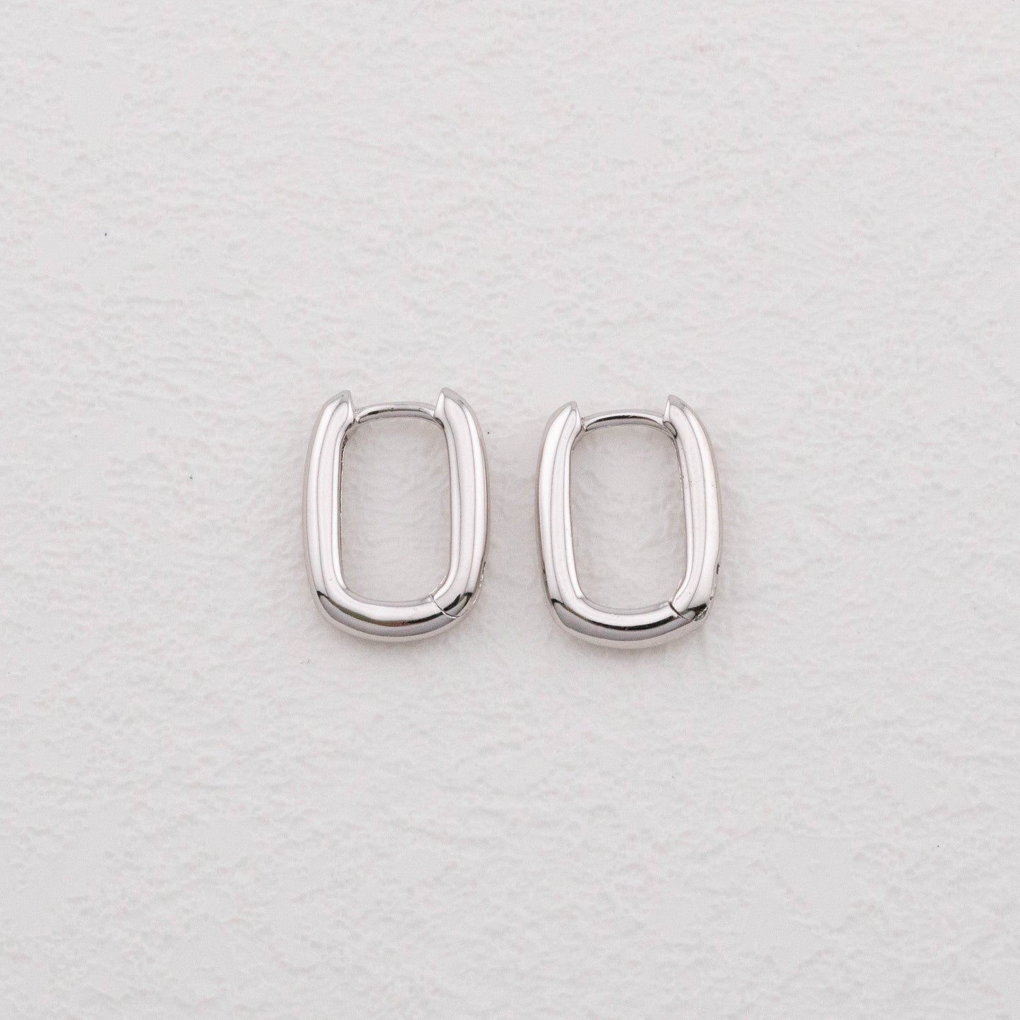 Mini chunky sterling silver rectangular hoop earrings on white surface, top view showing bold shape.