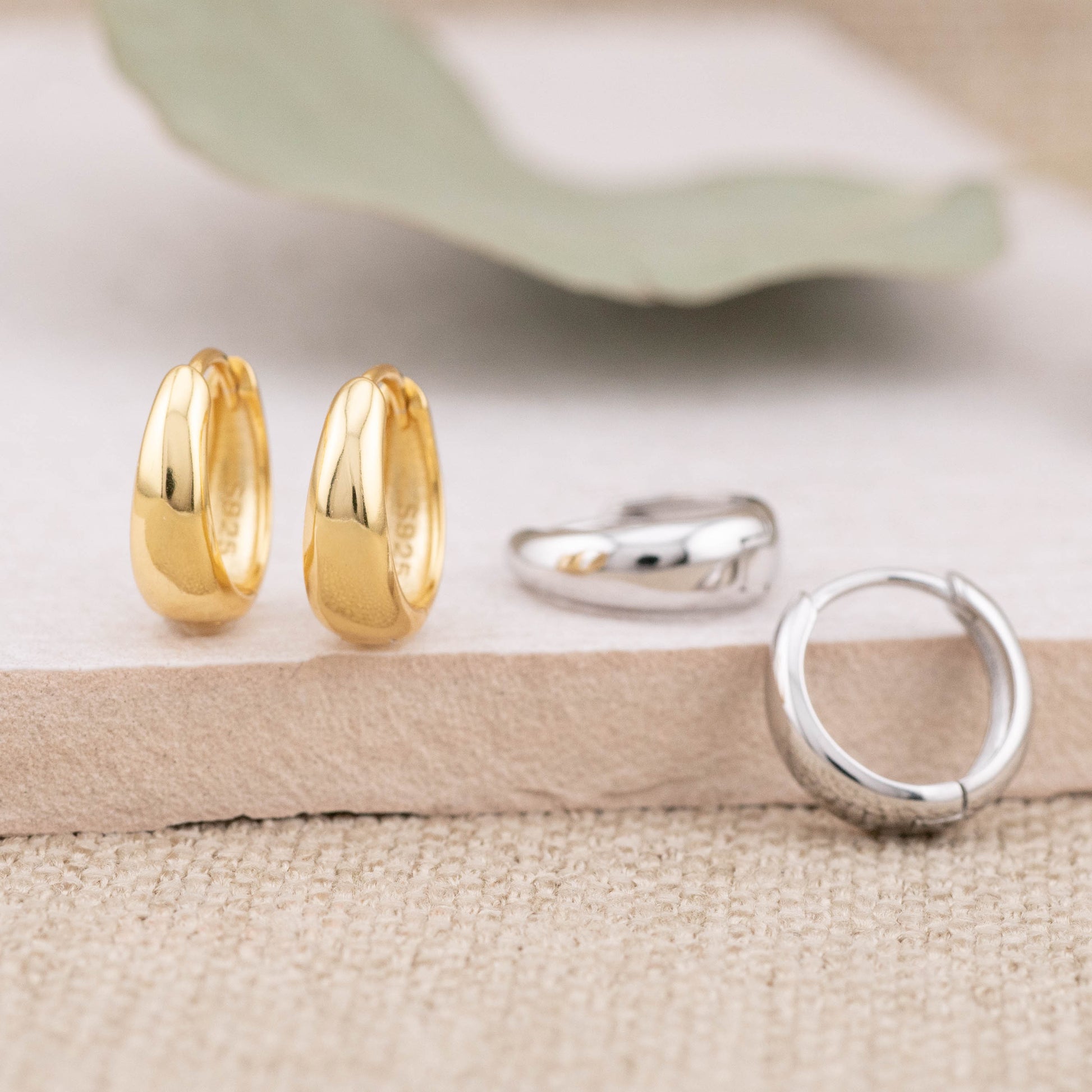 Gold and silver hoop earrings on a textured surface with a green leaf in the background.
