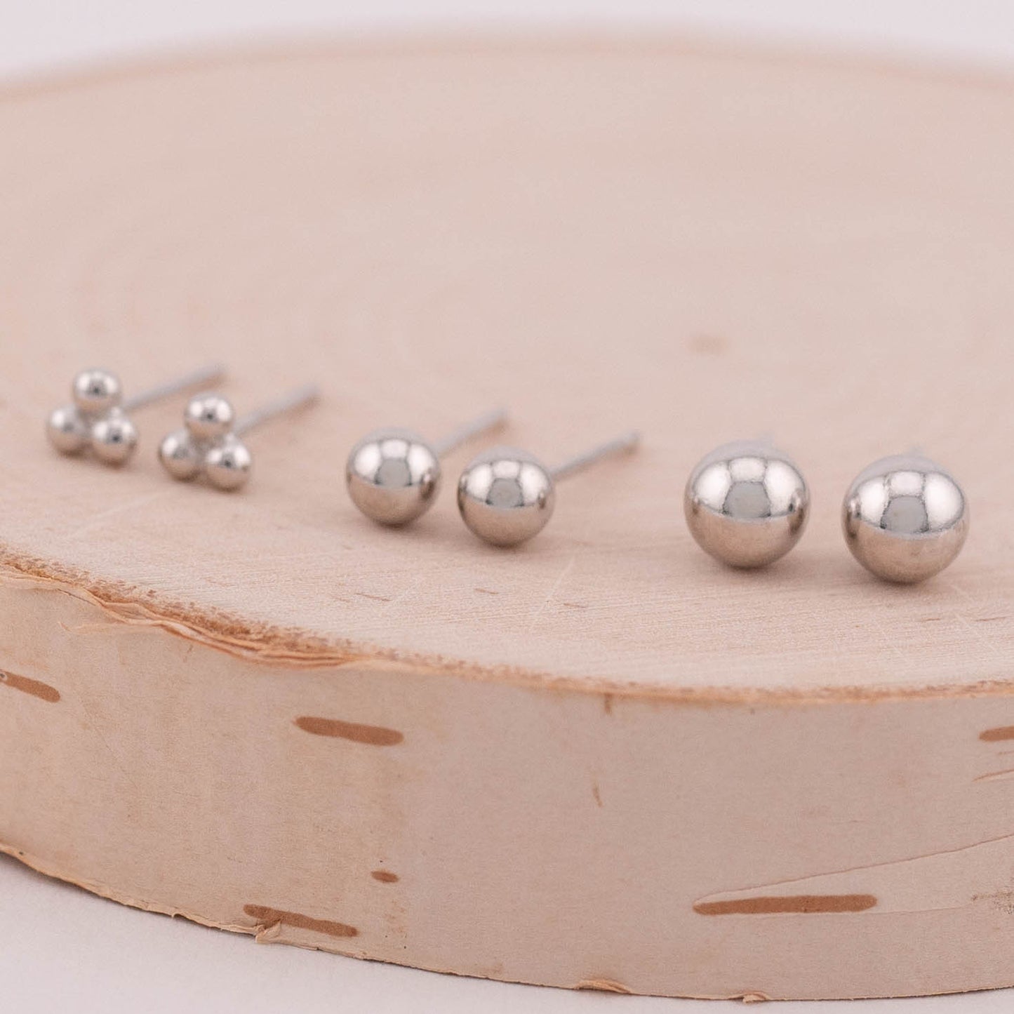 Three sets of silver ball stud earrings arranged side by side, captured from a 45-degree angle to reveal both the front and back of the earrings. A versatile choice for adding subtle elegance to any ensemble