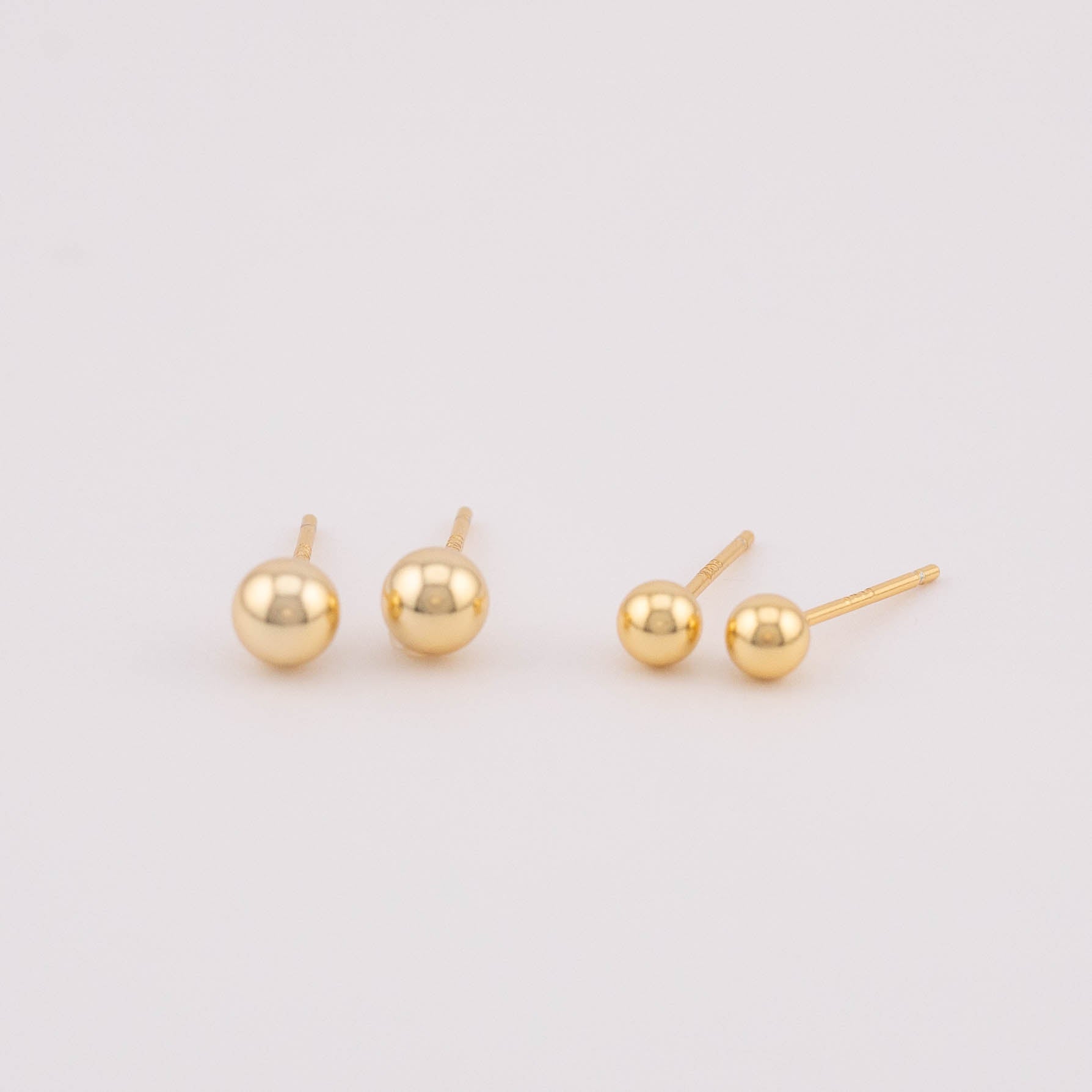 Front view photo displaying two sets of gold ball earrings with varying sizes, positioned side by side for easy comparison. Ideal for selling as a set, showcasing the versatility in size options and offering a stylish addition to any jewelry collection.