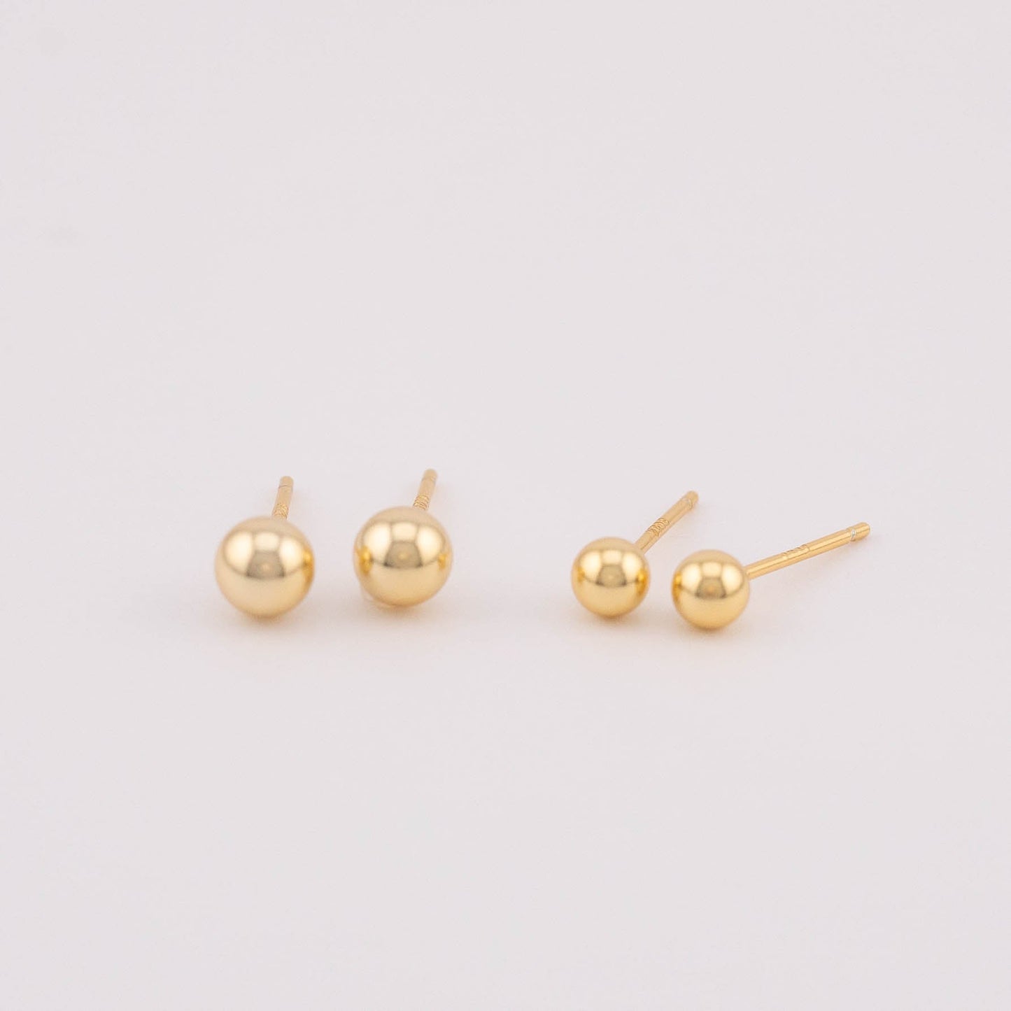Front view photo displaying two sets of gold ball earrings with varying sizes, positioned side by side for easy comparison. Ideal for selling as a set, showcasing the versatility in size options and offering a stylish addition to any jewelry collection.