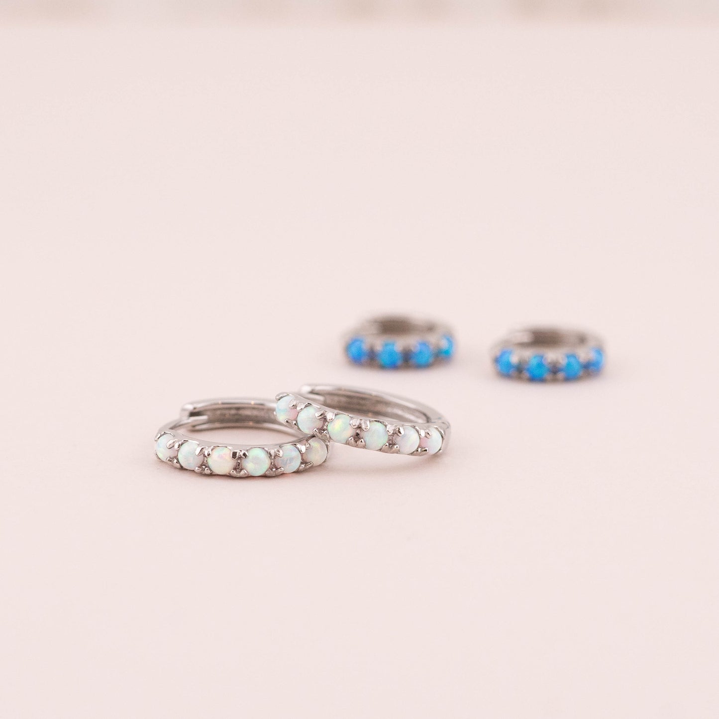 Close-up of small opal huggie hoops showcasing intricate white opal details. Blurred blue opal huggies in background add contrast