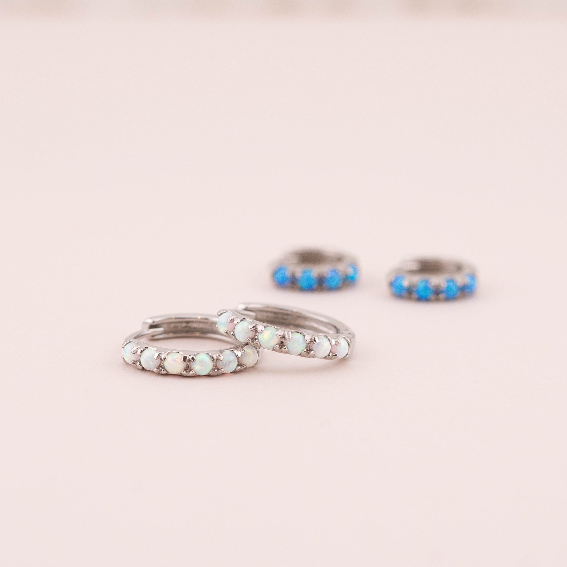 Close-up of small opal huggie hoops showcasing intricate white opal details. Blurred blue opal huggies in background add contrast