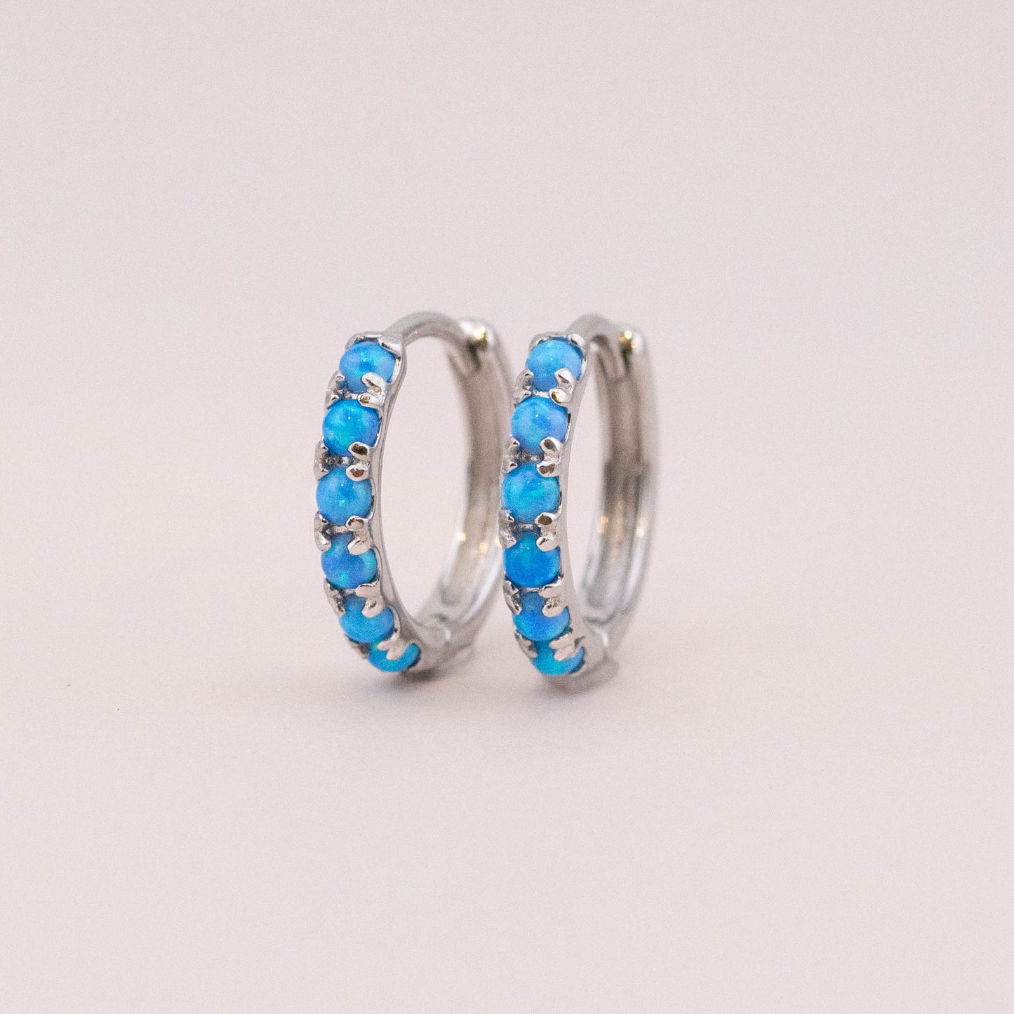 Sterling silver huggie earrings with vibrant fire blue opal stones, showcasing intricate details and captivating color against a light backdrop