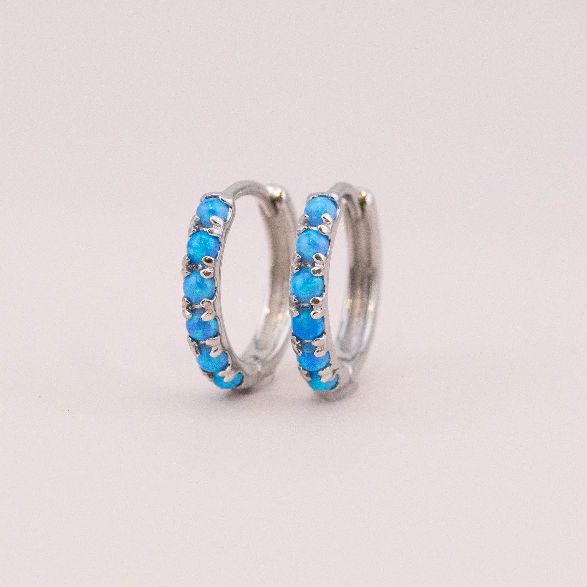 Sterling silver huggie earrings with vibrant fire blue opal stones, showcasing intricate details and captivating color against a light backdrop