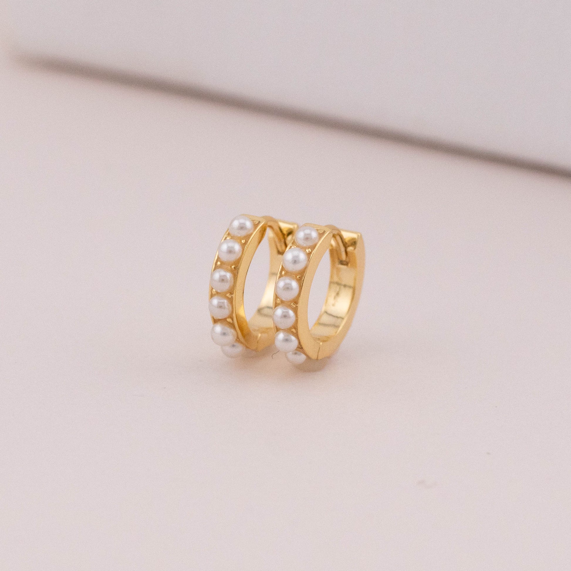 Chubby gold hoops with white pearls stones, shown from the side to highlight thickness.