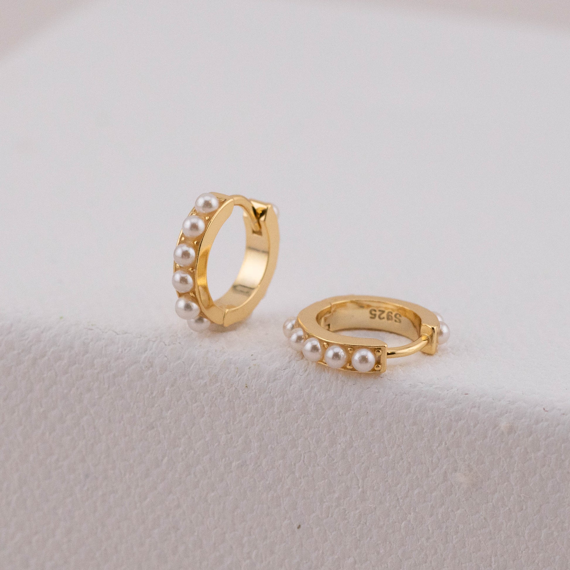 Bold huggie hoops in gold with white pearls, showing one laid down to highlight thickness.