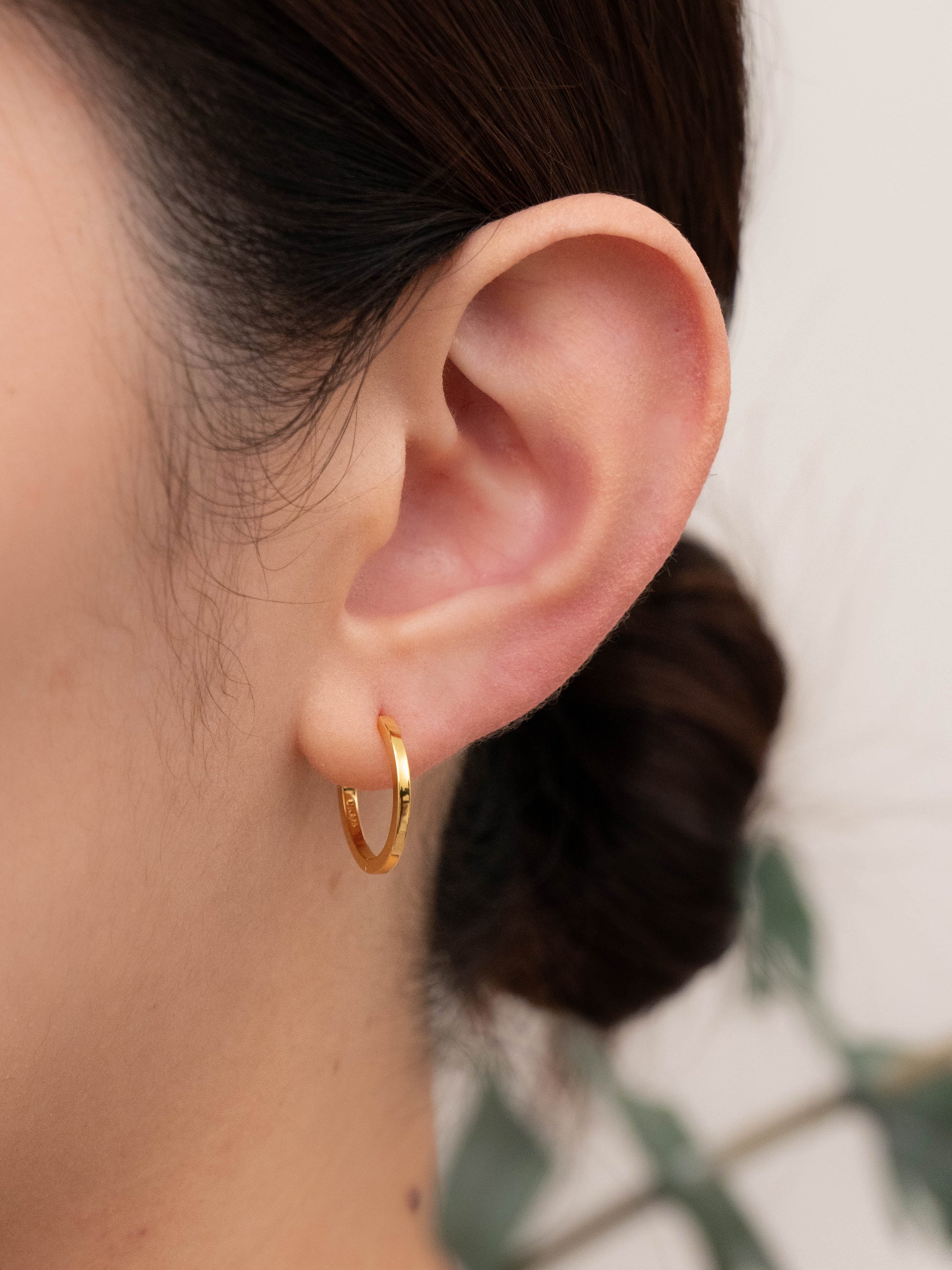 Small huggies gold on a model's ear, showing hinged closure and how they look when worn.