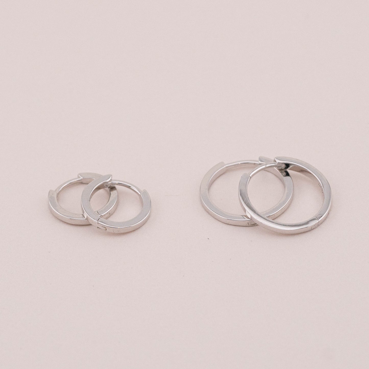 Two pairs of silver huggie hoop earrings, laid on a surface, showing different sizes for stacking.