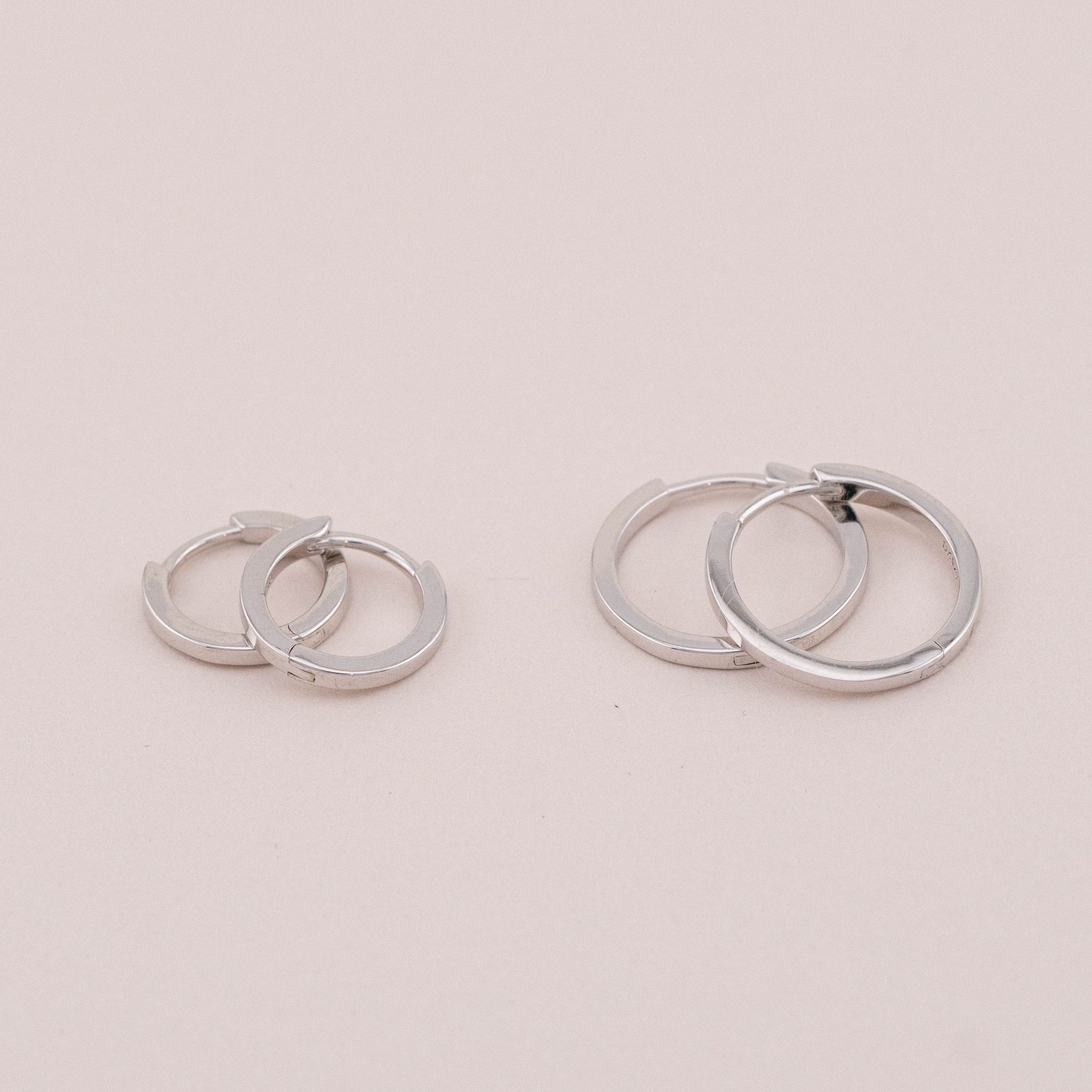 Two pairs of silver huggie hoop earrings, laid on a surface, showing different sizes for stacking.
