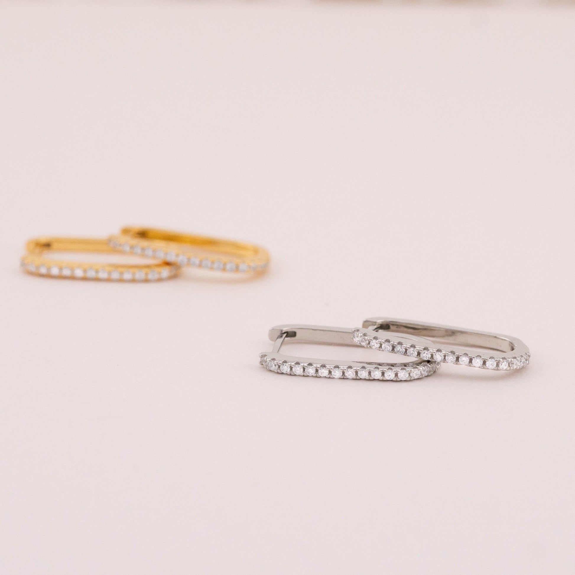 Close-up view of small square hoop earrings in gold and silver, highlighting their shimmering stones.