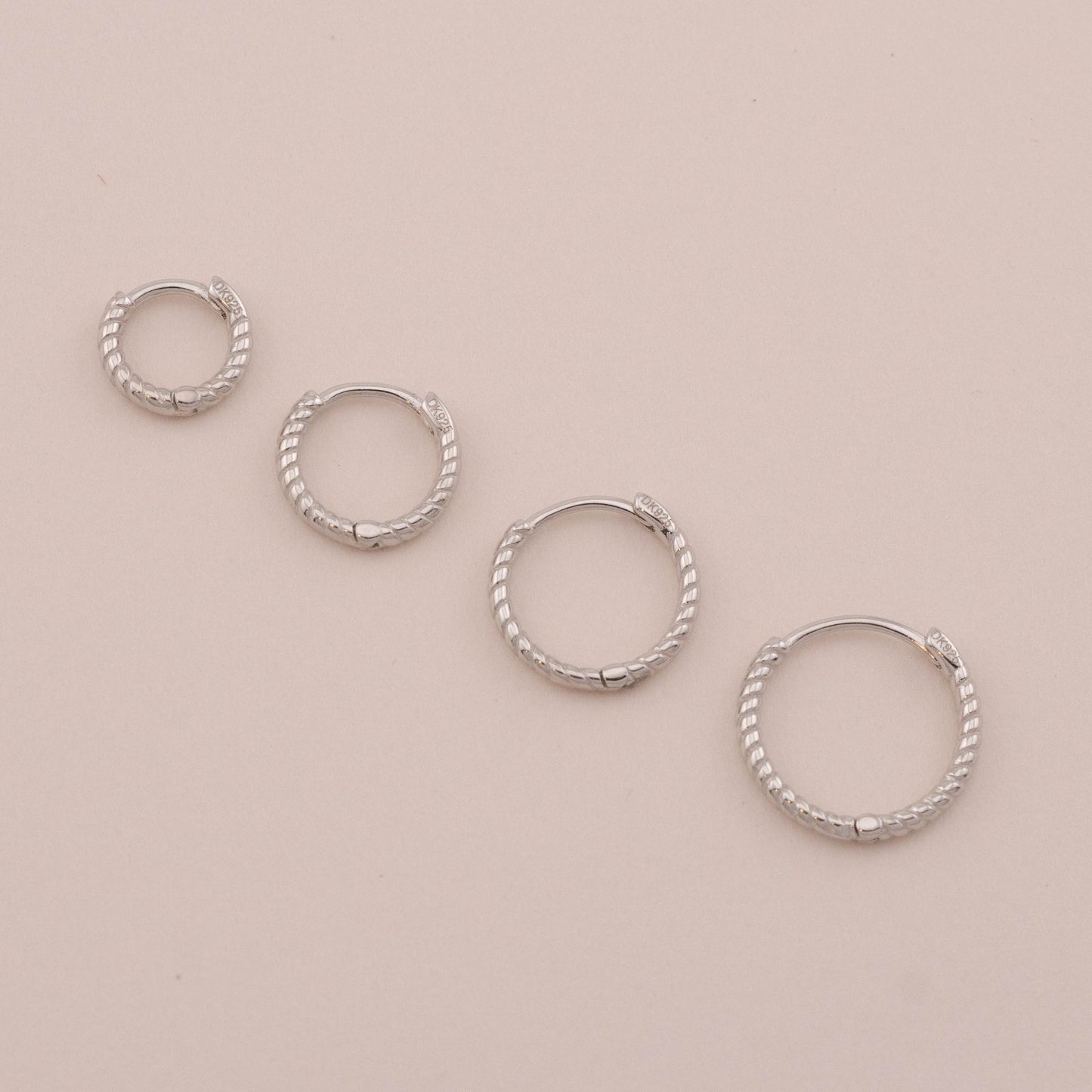 4 sizes of small huggie hoops laid down, showing hinged closures for everyday wear.
